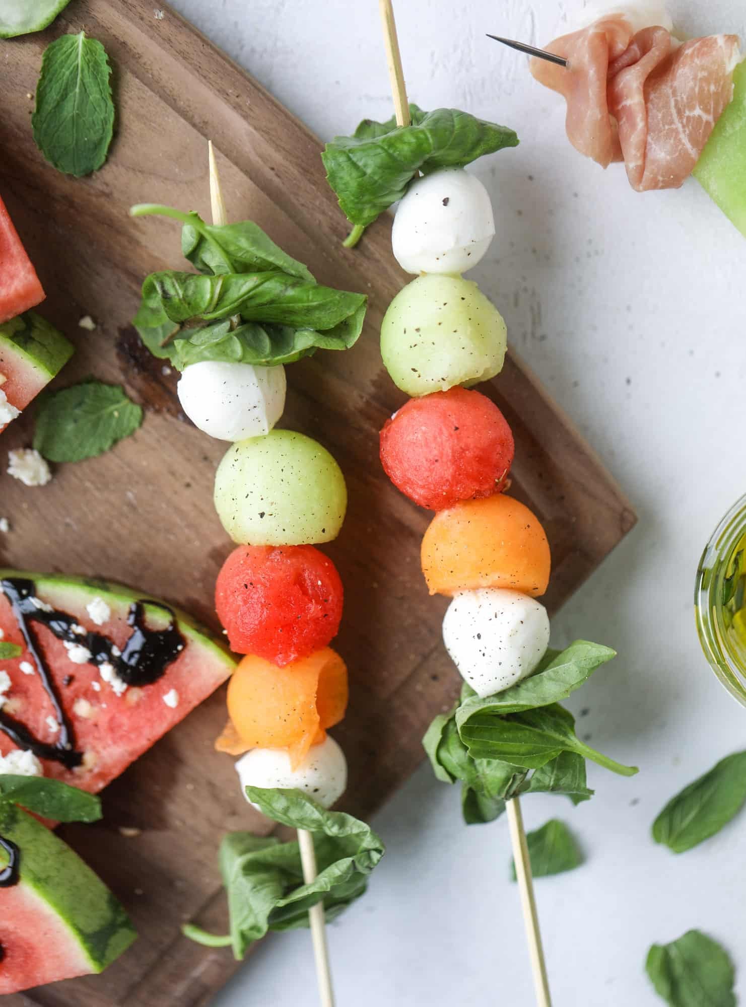 Create a melon summer snacking board with watermelon, cantaloupe, cucumber and honeydew. Drizzled with balsalmic, pesto, fresh herbs and paired with prosciutto and marinated mozzarella. I howsweeteats.com #melon #summer #snack #cheese #board #watermelon