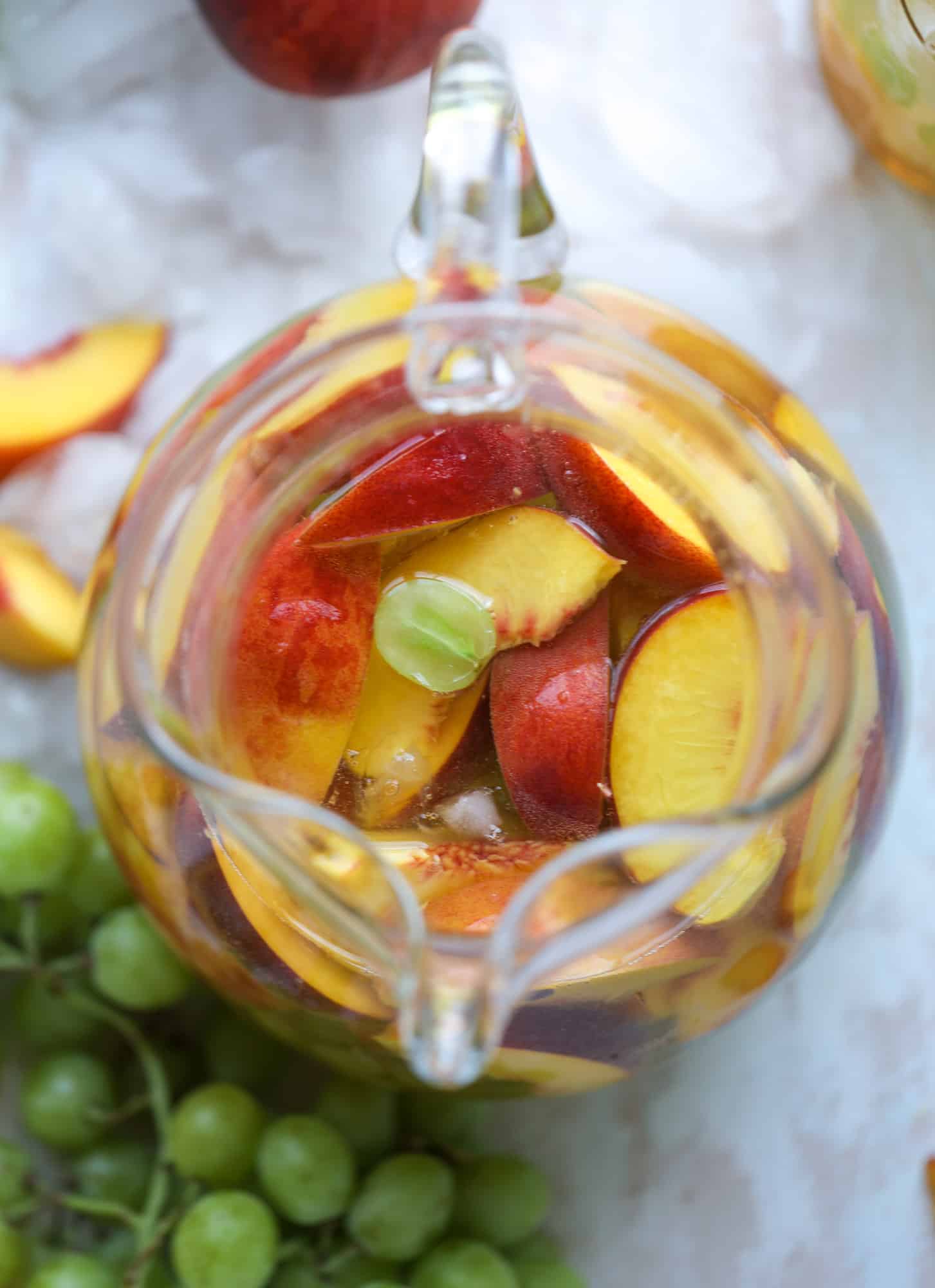 This pinot grigio sangria is absolutely perfect for summer, complete with peach nectar, fresh and frozen peach slices, brandy and bubbles! Frozen green grapes add some chill without watering down the drink. It's perfect! I howsweeteats.com #pinot #grigio #peach #sangria #cocktails #punch #summer #wine