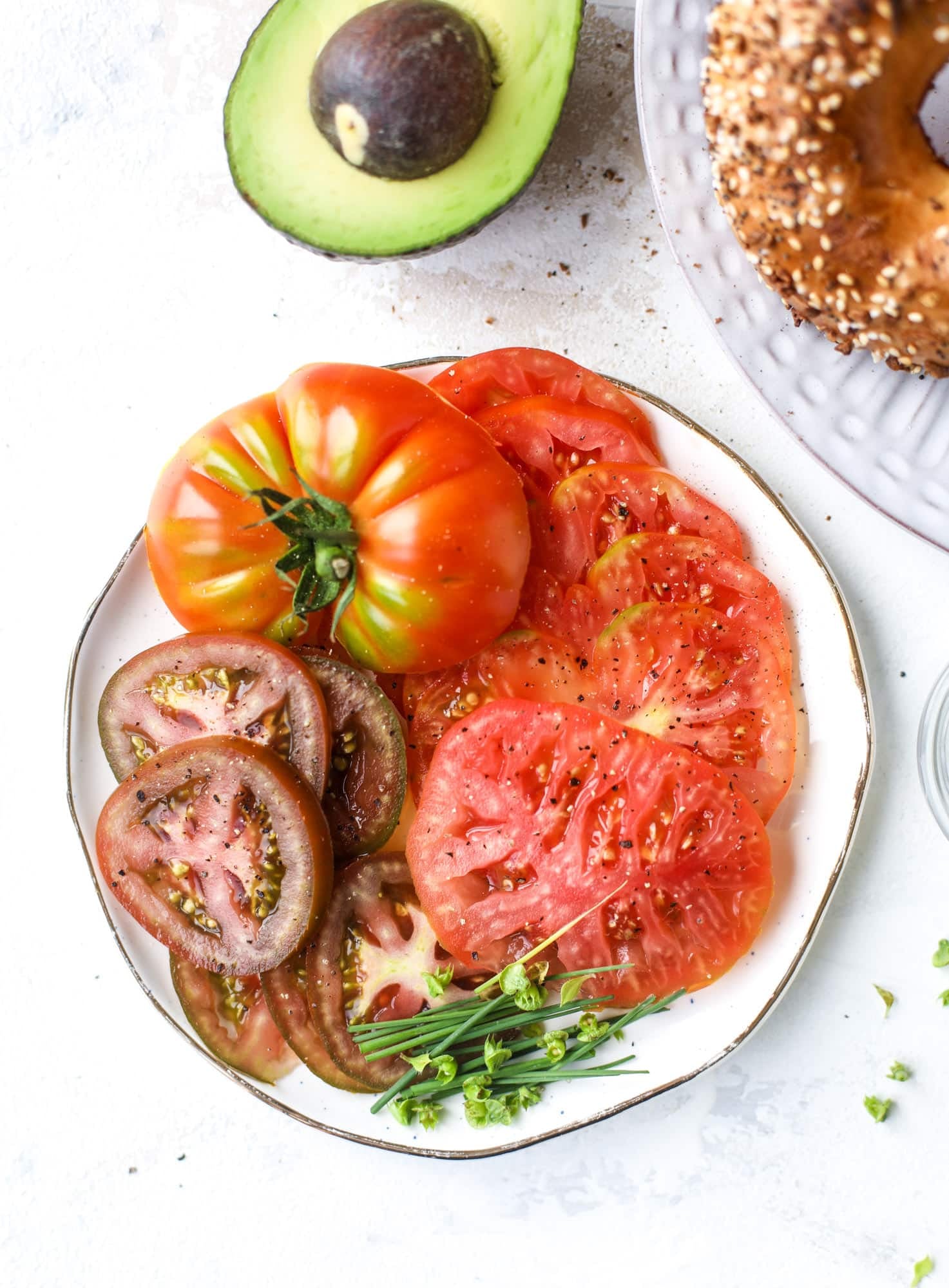 These avocado tomato sandwiches are the perfect lunch! Complete with veggie cream cheese, smoked sea salt, fresh chives and microgreens, the sliced avocado and heirloom tomatoes are sandwiched on an everything bagel for a flavor explosion. I howsweeteats.com #avocado #tomato #sandwich #healthy #lunch