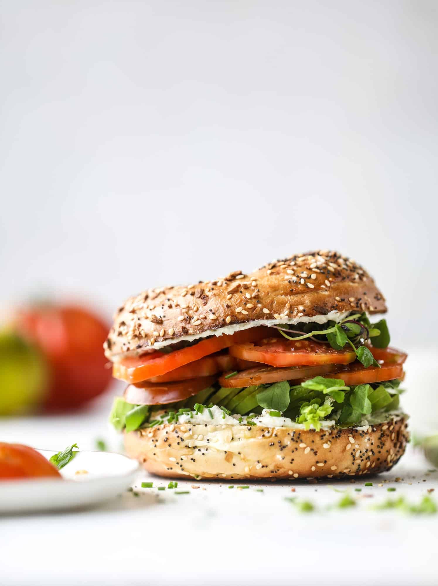 These avocado tomato sandwiches are the perfect lunch! Complete with veggie cream cheese, smoked sea salt, fresh chives and microgreens, the sliced avocado and heirloom tomatoes are sandwiched on an everything bagel for a flavor explosion. I howsweeteats.com #avocado #tomato #sandwich #healthy #lunch