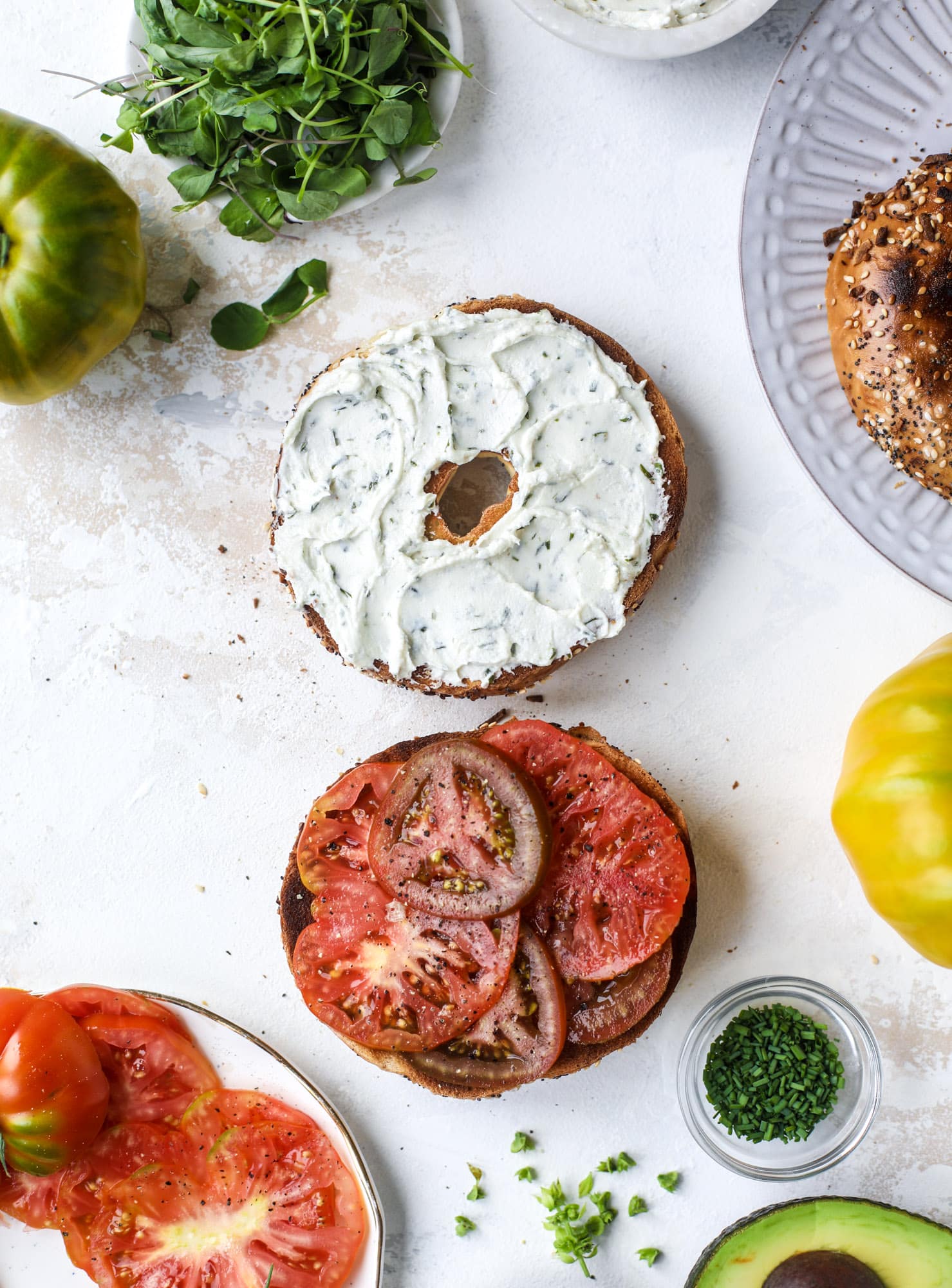 These avocado tomato sandwiches are the perfect lunch! Complete with veggie cream cheese, smoked sea salt, fresh chives and microgreens, the sliced avocado and heirloom tomatoes are sandwiched on an everything bagel for a flavor explosion. I howsweeteats.com #avocado #tomato #sandwich #healthy #lunch