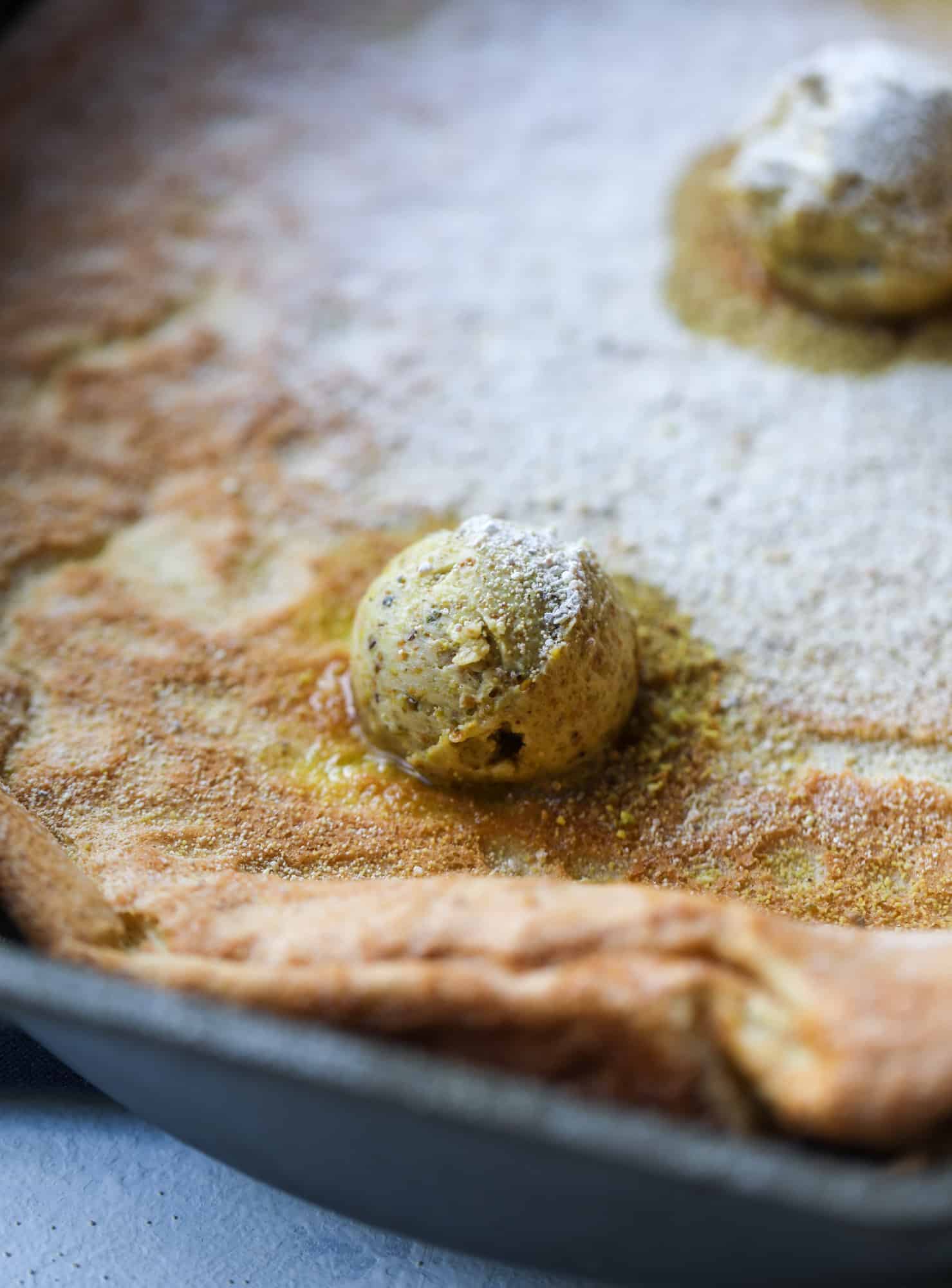 This incredible dutch baby recipe is fluffy and light and perfect for breakfast! It's sprinkled with pistachio sugar and served with pistachio butter and fresh blueberries. It's super easy, simple and always a hit! I howsweeteats.com #dutch #baby #pistachio #blueberry #breakfast