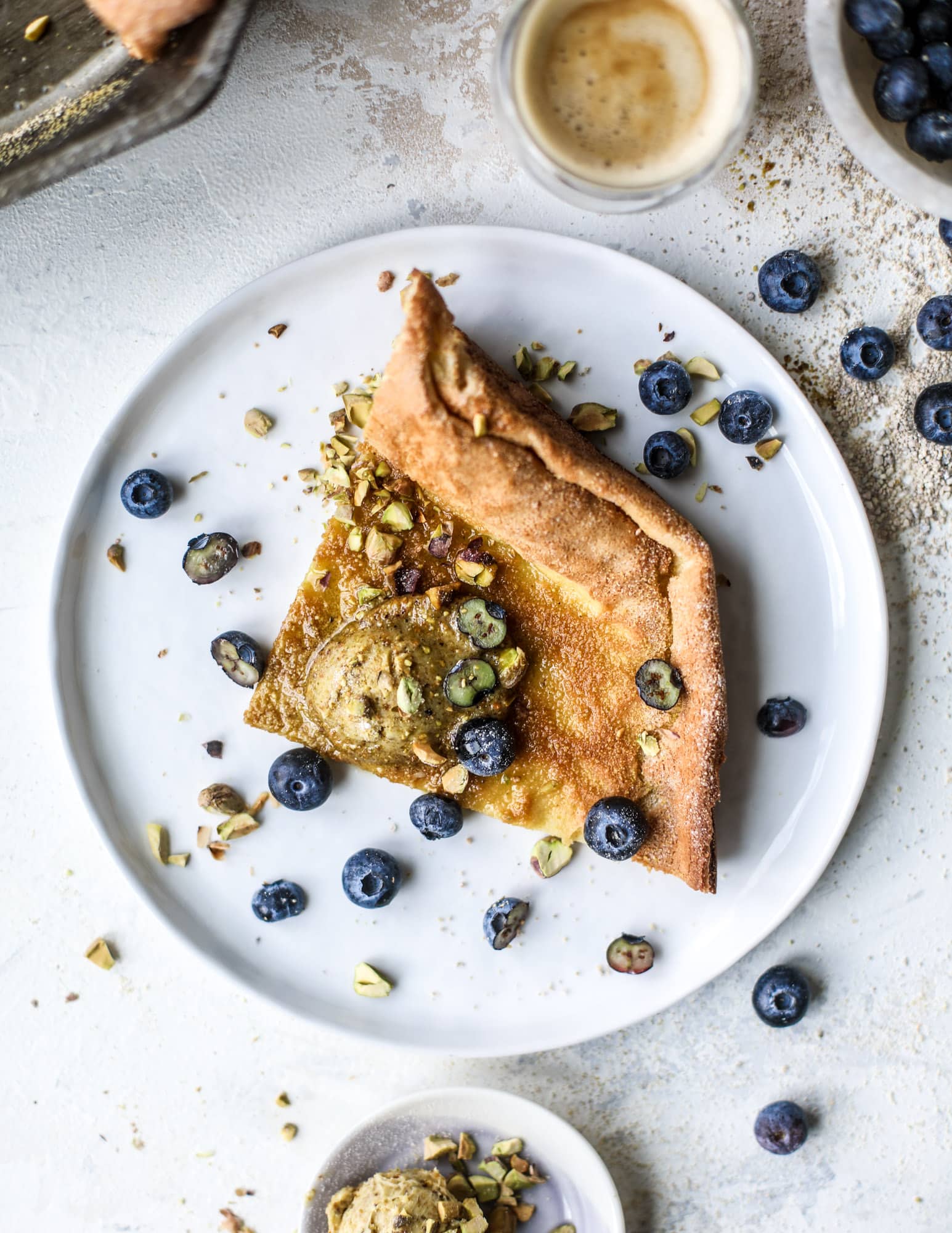 This incredible dutch baby recipe is fluffy and light and perfect for breakfast! It's sprinkled with pistachio sugar and served with pistachio butter and fresh blueberries. It's super easy, simple and always a hit! I howsweeteats.com #dutch #baby #pistachio #blueberry #breakfast
