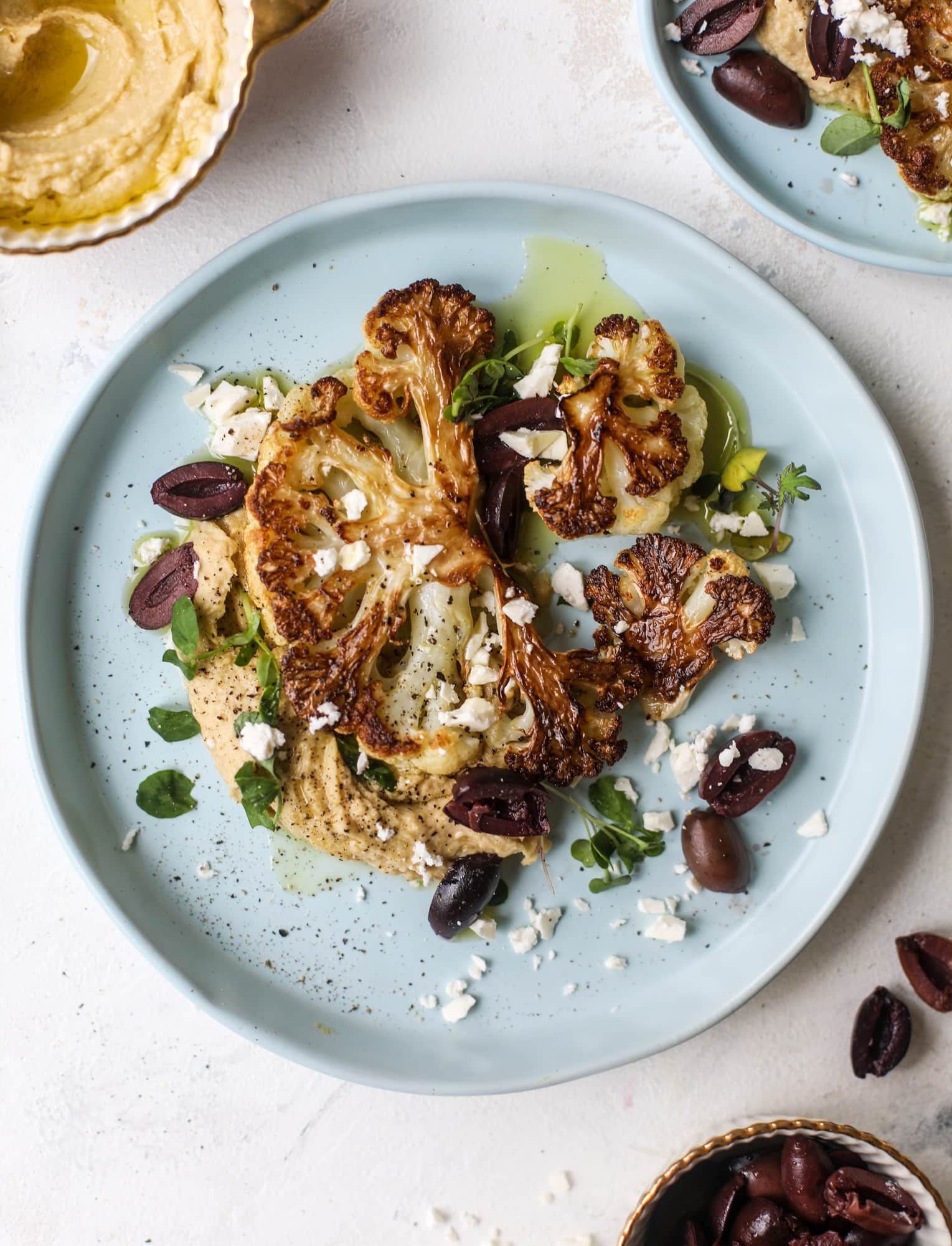 This roasted cauliflower with hummus, olives and feta is super flavorful and a wonderful meal, side dish or snack. Flavorful roasted cauliflower, creamy hummus, briney olives and tangy feta come together to make a major taste explosion. I howsweeteats.com #roasted #cauliflower #hummus #olives #feta