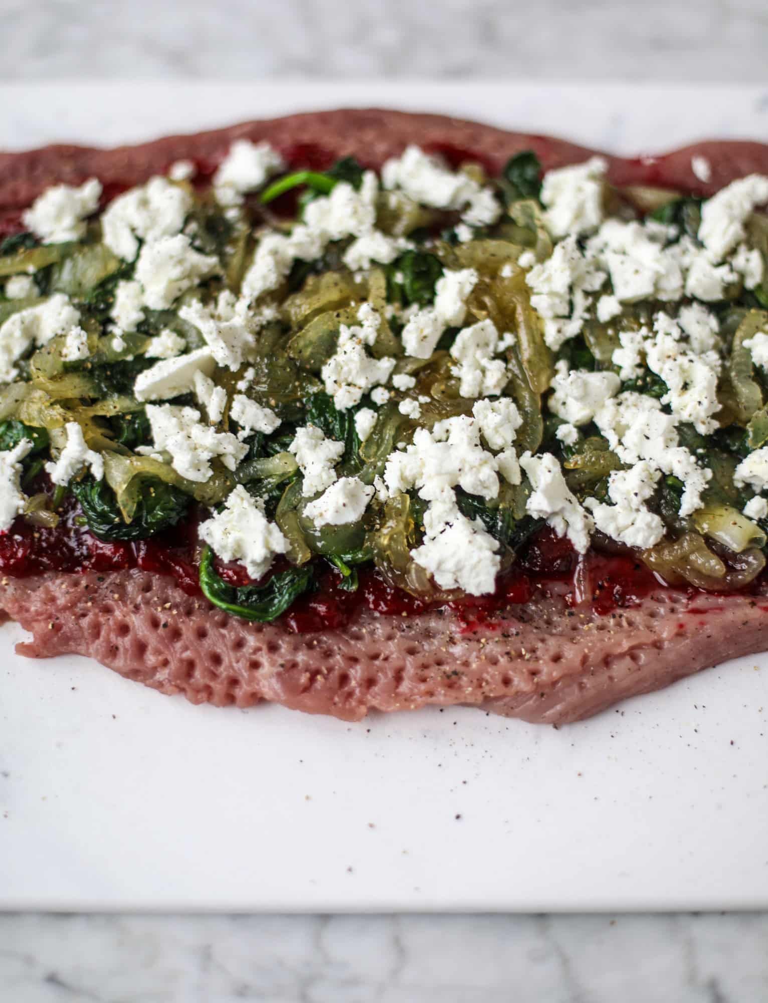 This holiday stuffed pork tenderloin is filled with caramelized onion, fresh cranberry sauce, goat cheese and fresh spinach. It's a show stopped and super delicious, along with being fairly simple to make! I howsweeteats.com #stuffed #porktenderloin