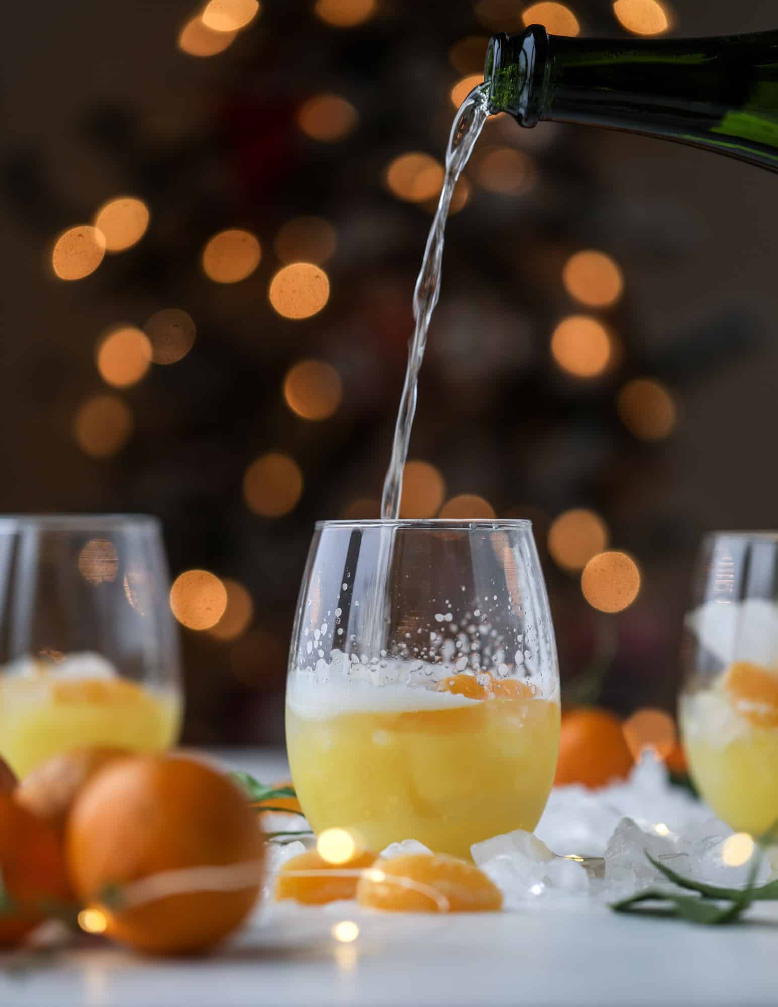 This satsuma cocktail is perfect for the holiday season and winter months when sweet satsumas are in season! This cocktail uses gin or vodka and is topped with champagne and garnished with a few satsuma wedges. Delicious! I howsweeteats.com #satsuma #cocktail