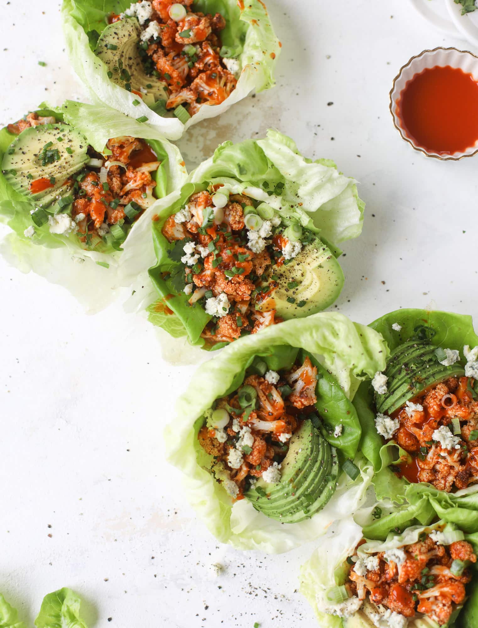 These buffalo cauliflower lettuce wraps are perfect for game day or even a quick weeknight dinner. Roasted cauliflower with buffalo wing sauce, sliced avocado, crumbled blue cheese, scallions, cilantro and chives makes for a flavor explosion! I howsweeteats.com #buffalo #cauliflower