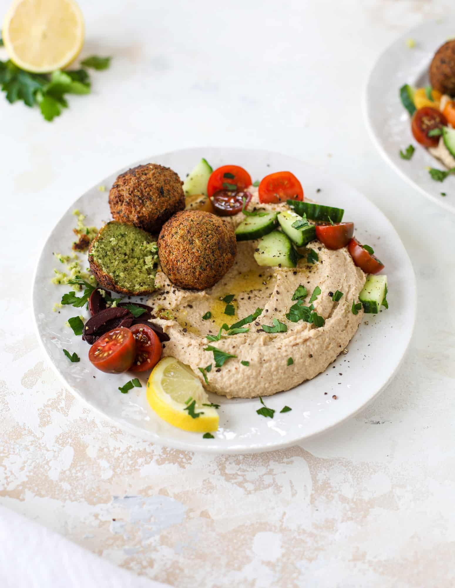Green goddess falafel is hearty and flavorful, served over the creamiest cauliflower hummus, with tomatoes, olive, cucumbers and feta. Yum! I howsweeteats.com #falafel #cauliflowerhummus