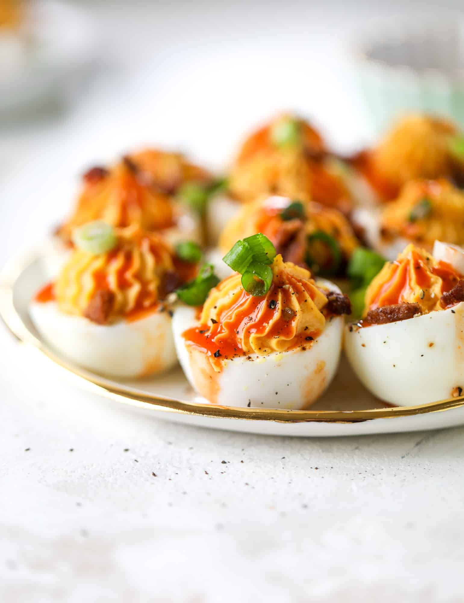Buffalo deviled eggs are kicked-up deviled eggs! Made with goat cheese filling and served with buffalo wing sauce, crispy bacon and sliced scallions. I howsweeteats.com #deviledeggs #buffalo