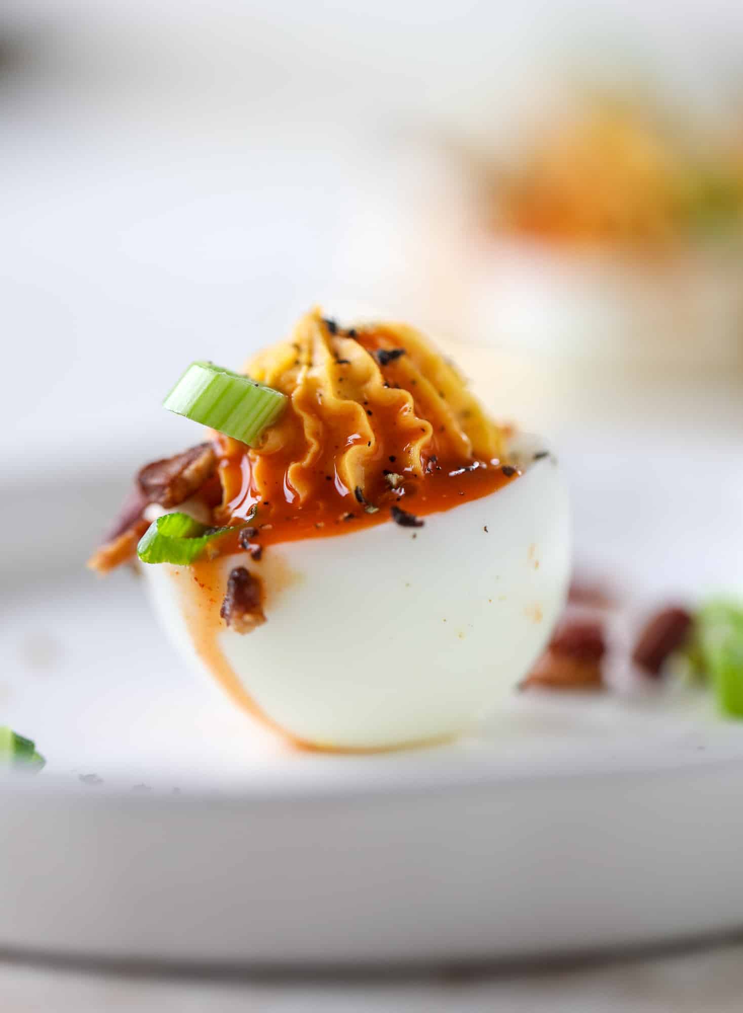Buffalo deviled eggs are kicked-up deviled eggs! Made with goat cheese filling and served with buffalo wing sauce, crispy bacon and sliced scallions. I howsweeteats.com #deviledeggs #buffalo