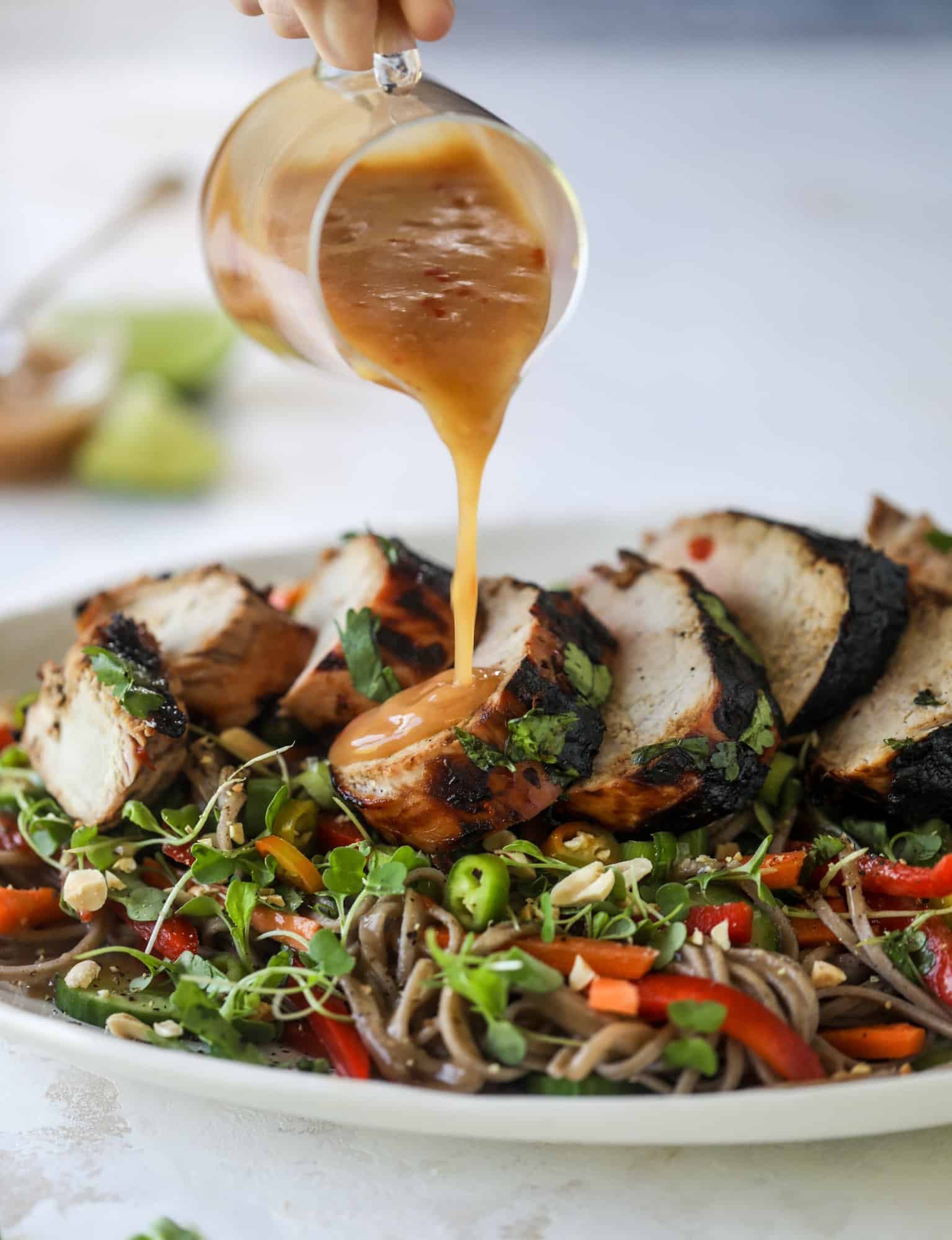 This grilled thai pork tenderloin is so easy, super flavorful, and the perfect weeknight meal when you serve it with a soda noodle salad. pouring peanut sauce on grilled pork tenderloin