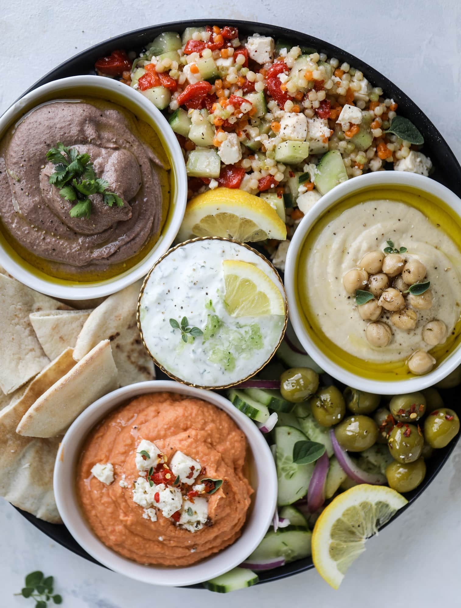 Here you can find out how to make the perfect hummus platter! This trio includes caramelized onion hummus, smoky black bean hummus and roasted red pepper white bean hummus, along with a couscous salad and quick tzatziki! I howsweeteats.com #hummus #platter #appetizer #snack #chickpeas #healthy #blackbeans #yogurt #tzatziki