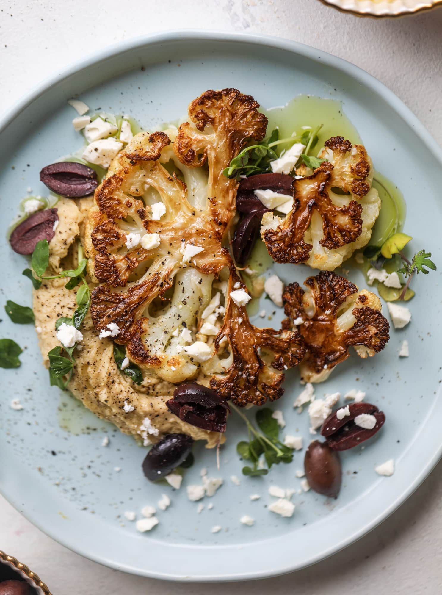 This roasted cauliflower with hummus, olives and feta is super flavorful and a wonderful meal, side dish or snack. Flavorful roasted cauliflower, creamy hummus, briney olives and tangy feta come together to make a major taste explosion. I howsweeteats.com #roasted #cauliflower #hummus #olives #feta