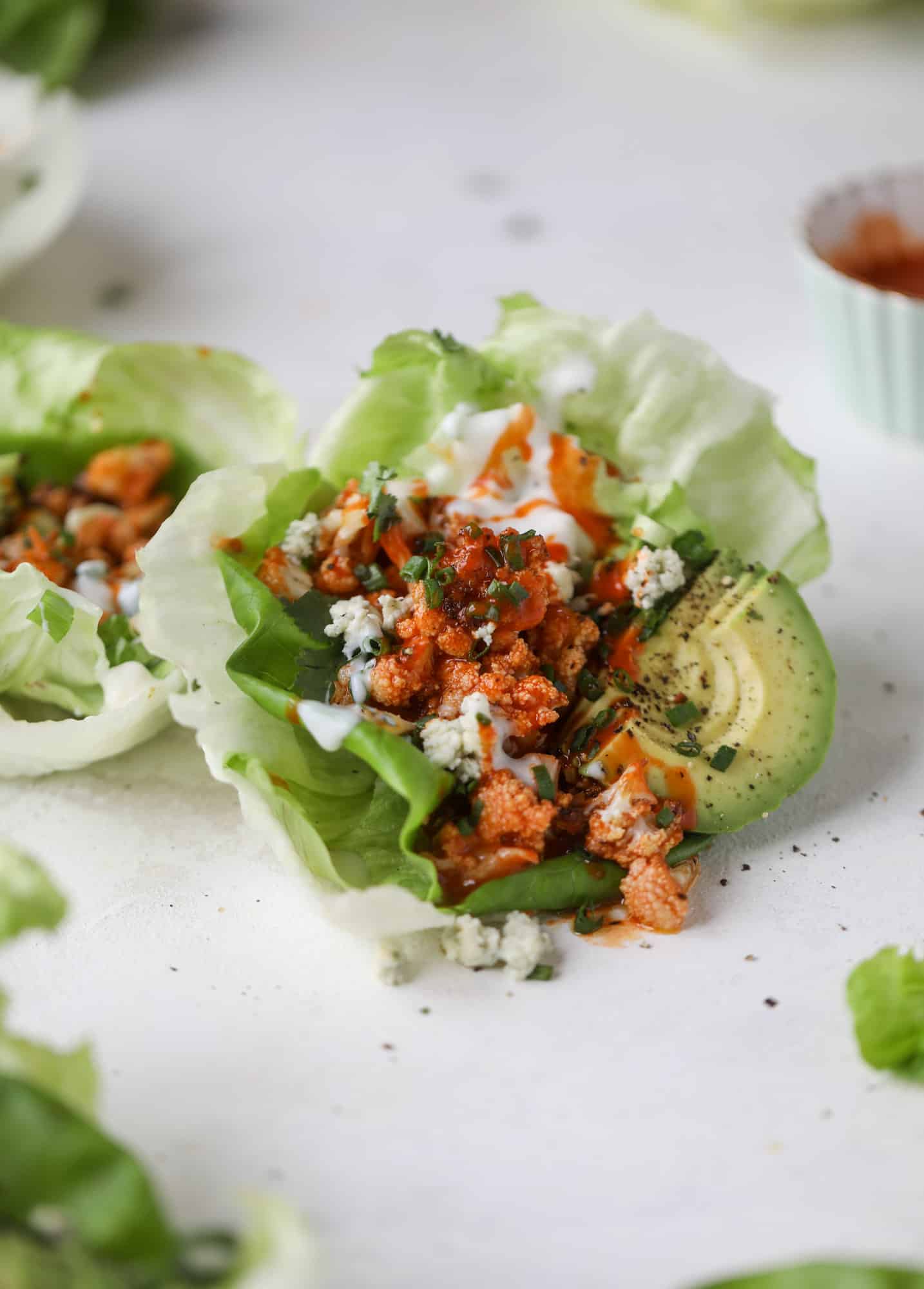 These buffalo cauliflower lettuce wraps are perfect for game day or even a quick weeknight dinner. Roasted cauliflower with buffalo wing sauce, sliced avocado, crumbled blue cheese, scallions, cilantro and chives makes for a flavor explosion! I howsweeteats.com #buffalo #cauliflower