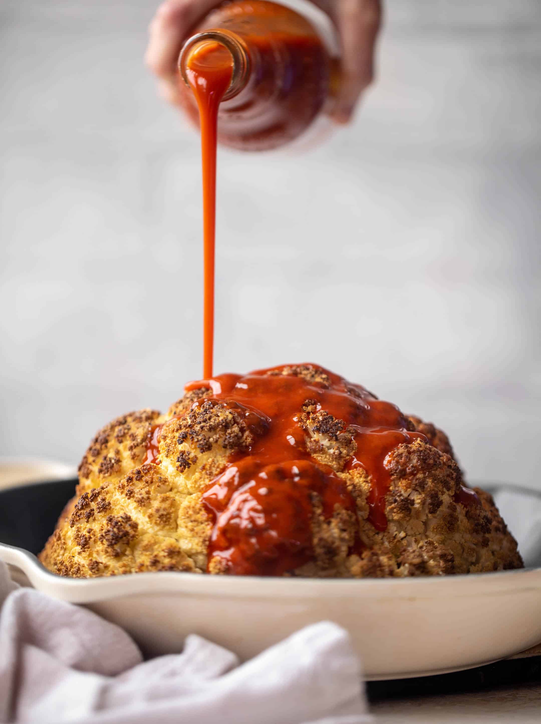 pouring buffalo sauce on whole cauliflower